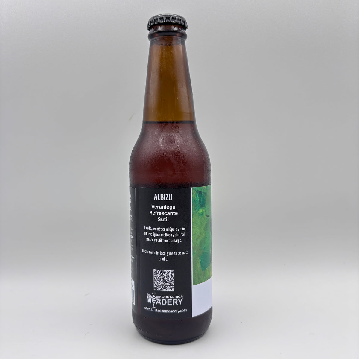 Vista lateral de la botella de Cerveza Albizu mostrando en la etiqueta la descripción Veraniega, Refrescante y Sutil junto con un código QR sobre un fondo neutro.
