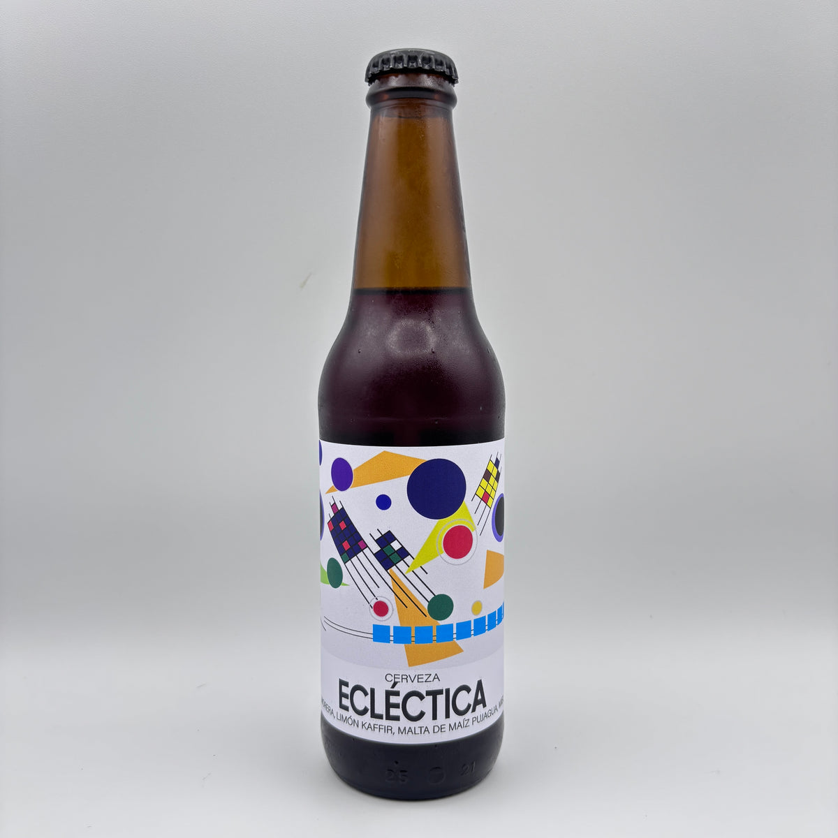 Botella de Cerveza Ecléctica con limón kaffir y malta de maíz, mostrando una etiqueta blanca con figuras geométricas de colores sobre un fondo neutro.
