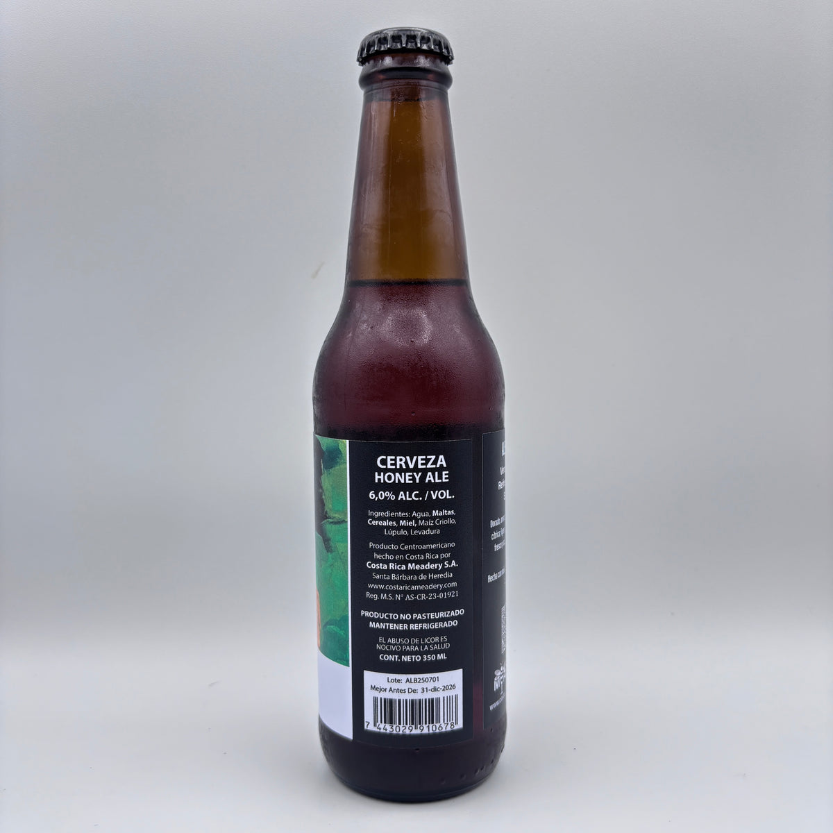 Vista trasera de la botella de Cerveza Honey Ale mostrando el porcentaje de alcohol (6.0% Alc/Vol), información del producto y código de barras sobre un fondo neutro.