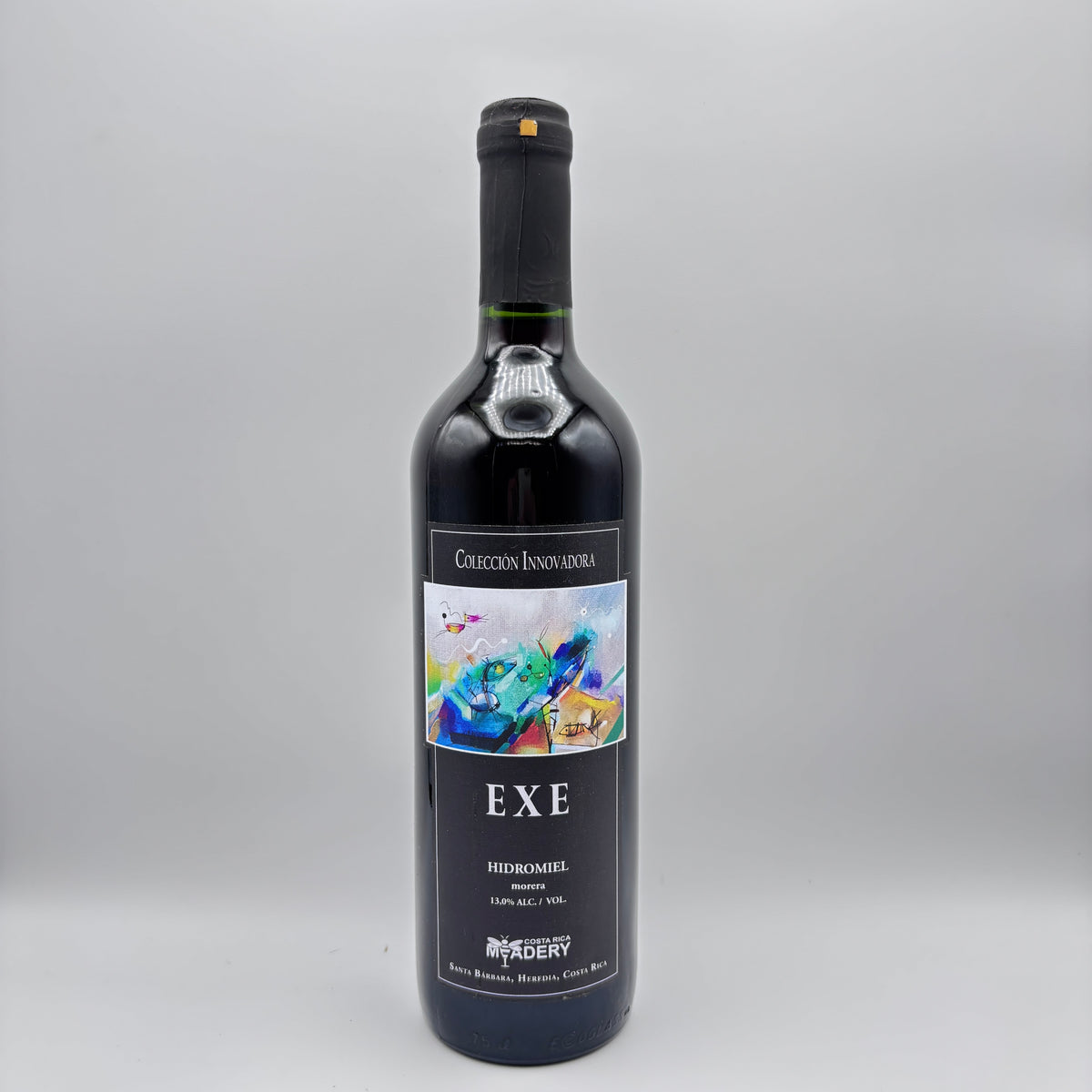 Botella de hidromiel Exe de la Colección Innovadora con etiqueta oscura e ilustración artística multicolor sobre un fondo neutro.