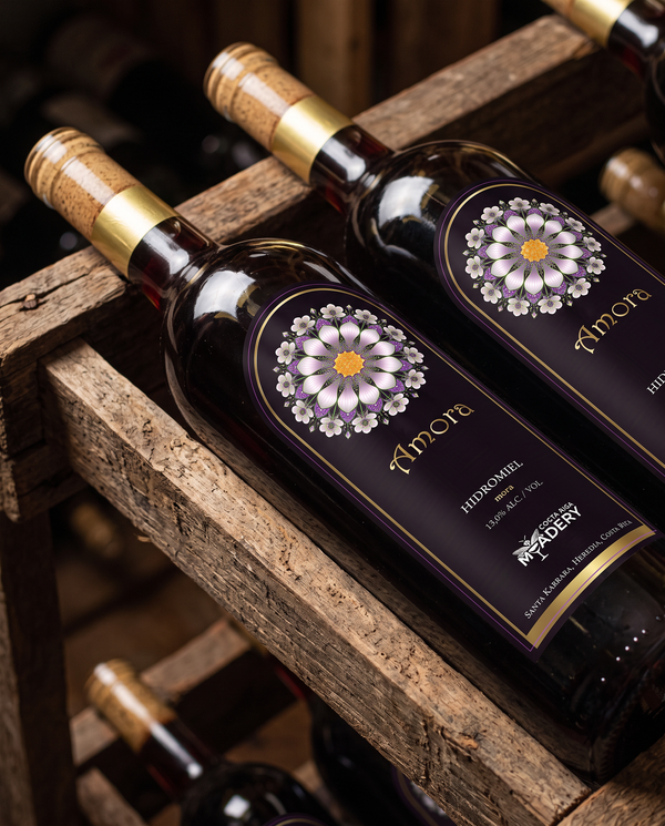 Dos botellas de hidromiel de mora marca Amora, de Costa Rica Meadery, reposando en posición inclinada sobre un estante de madera rústica estilo cava.