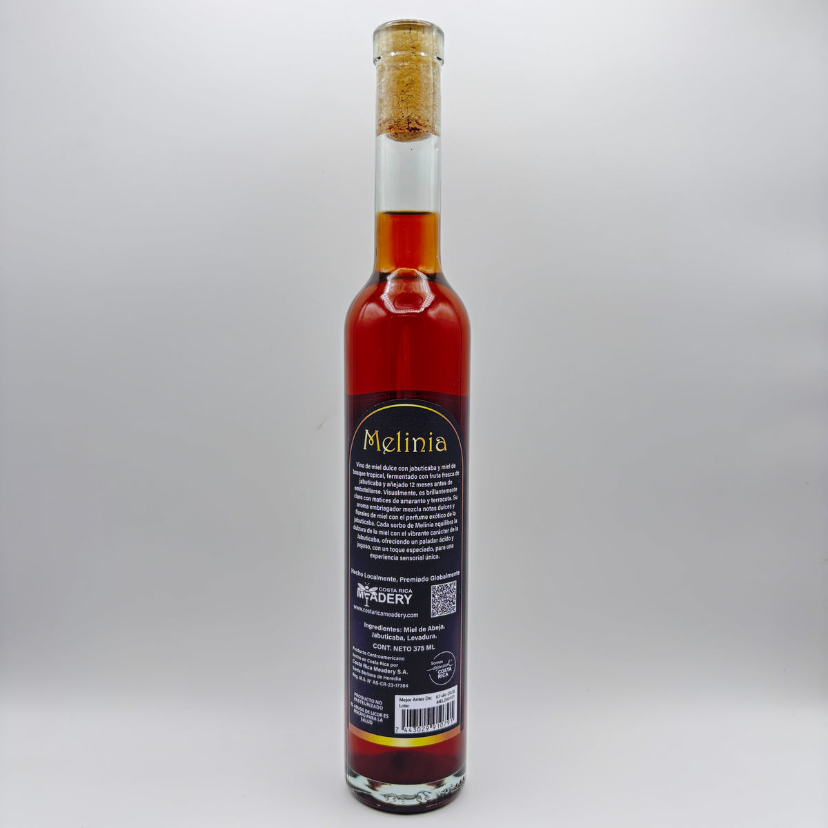 Vista trasera de la botella de hidromiel Melinia mostrando la contraetiqueta con la descripción del producto, el logo de Costa Rica Meadery y el código de barras sobre un fondo neutro.