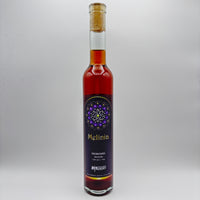 Botella estilizada de hidromiel Melinia con jaboticaba, mostrando una etiqueta oscura con un diseño mandálico morado y dorado sobre un fondo neutro.
