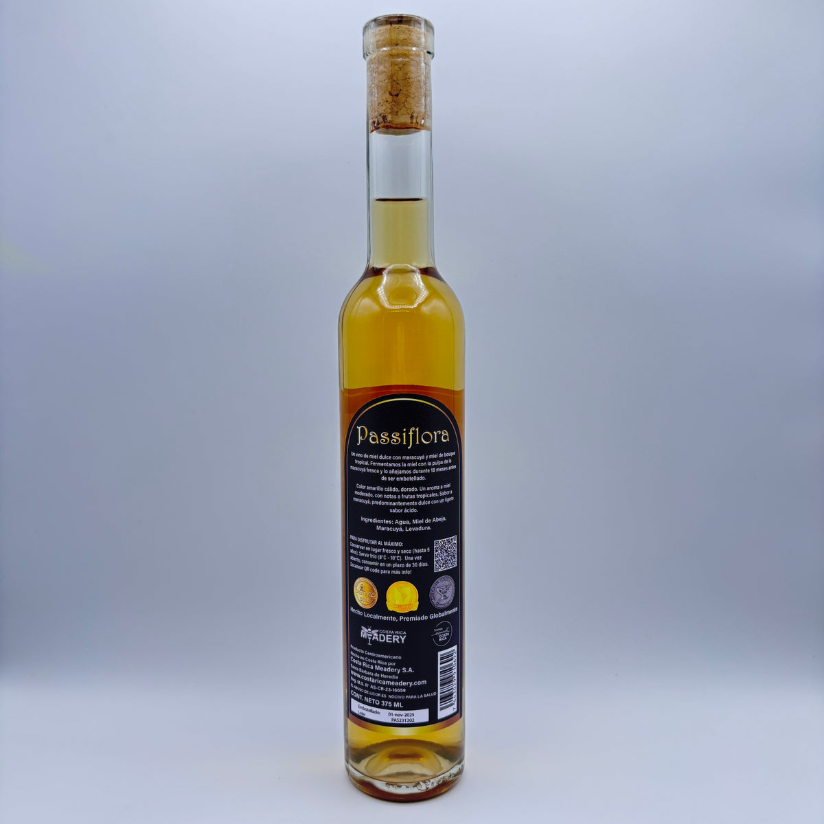 Vista trasera de la botella de hidromiel Passiflora mostrando la contraetiqueta con la descripción del producto, tres sellos de medallas obtenidas, el logo de Costa Rica Meadery y el código de barras sobre un fondo neutro.