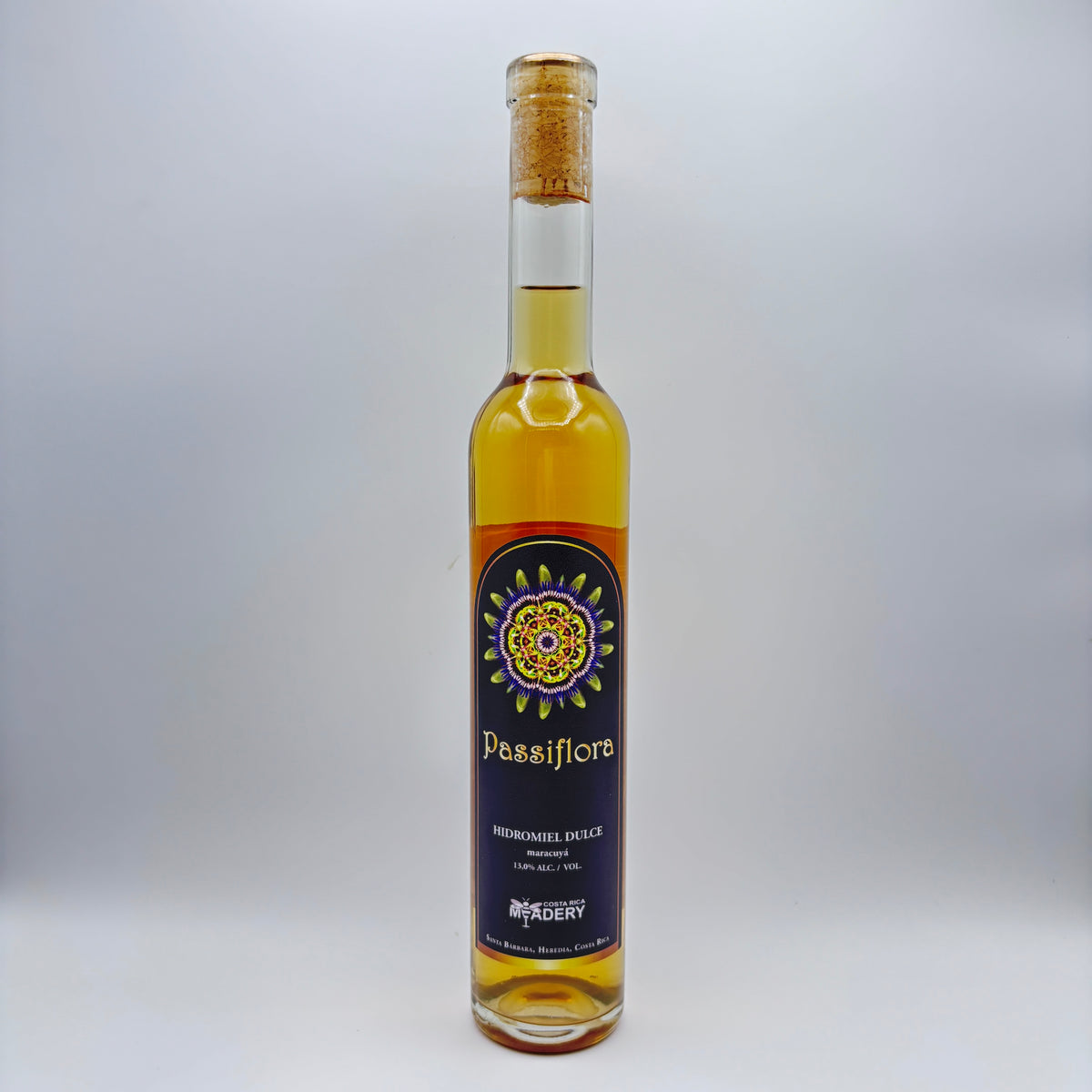 Botella estilizada de hidromiel dulce Passiflora con maracuyá, mostrando una etiqueta oscura con un diseño de mandala multicolor y el logo de Costa Rica Meadery sobre un fondo neutro.