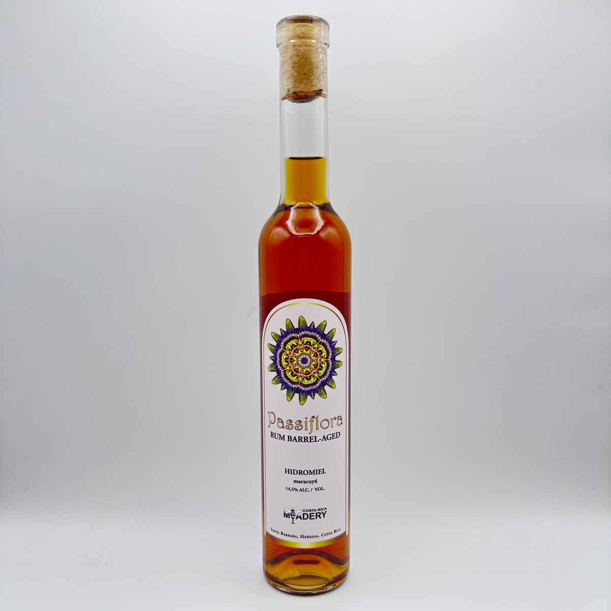 Botella estilizada de hidromiel Passiflora Rum Barrel-Aged con maracuyá, mostrando una etiqueta clara con un diseño mandálico multicolor y el logo de Costa Rica Meadery sobre un fondo neutro.